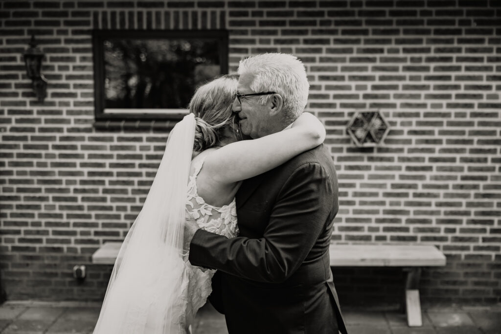 Emotionele zwart-wit foto van bruid die haar vader omhelst buiten bij Kasteel Ruurlo, trouwfotograaf Achterhoek