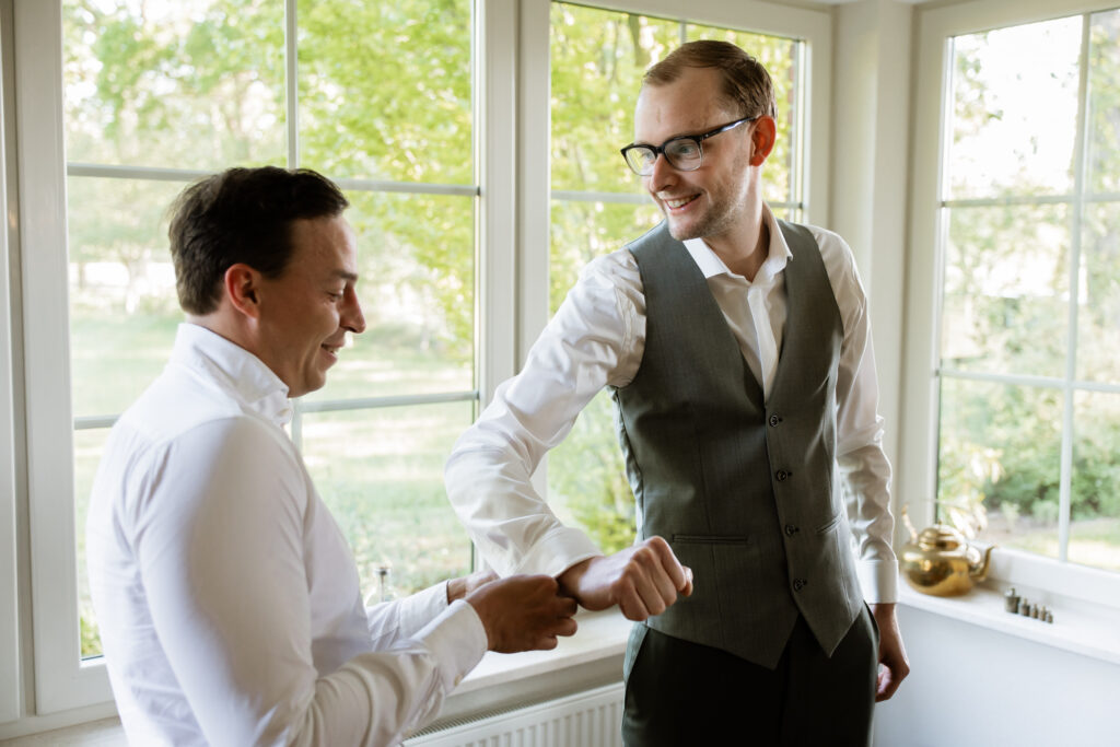 Bruidegom lacht met zijn getuige tijdens het aankleden voor de bruiloft, spontaan moment getting ready Kasteel Ruurlo