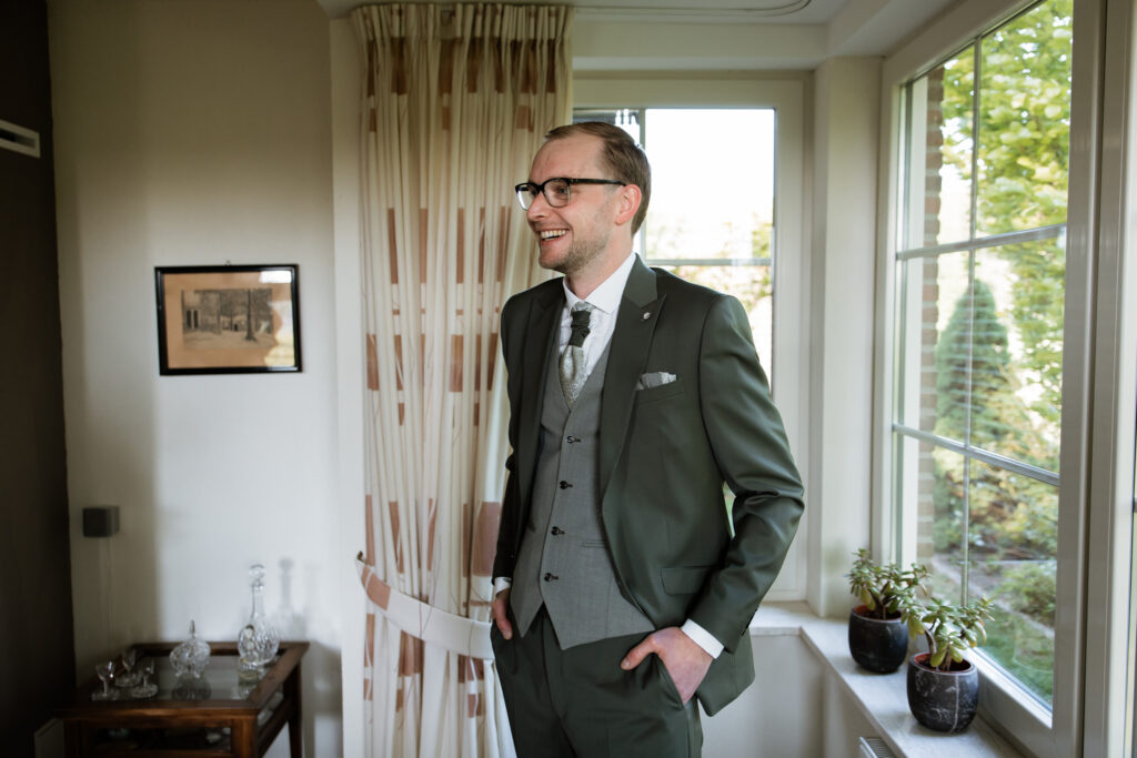 Bruidegom in groen driedelig pak bij raam during getting ready, trouwfotografie Kasteel Ruurlo Achterhoek